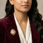 Woman wearing a burgundy blazer with a red and ivory cameo brooch, against a neutral background