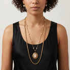 Woman in a black top wearing two necklaces, one with faux pearl accents on a gold tone chain and a red and ivory cameo pendant, the other a plain gold tone chain necklace. 