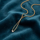 Gold tone Crystal Tweezer Pendant Necklace resting on a dark teal fabric 