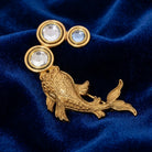 Gold fish-shaped brooch with crystals on a blue velvet background