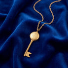 Gold tone Skeleton Key Flower Pendant Photo Locket Necklace resting on blue fabric 