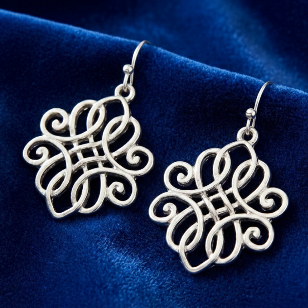Silver intricate earrings on a blue velvet background