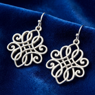 Silver intricate earrings on a blue velvet background