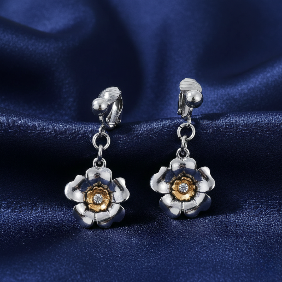 Silver flower-shaped earrings with gold details and a clear crystal in the middle on a blue satin background