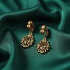 Gold earrings with green gemstones on a green fabric background