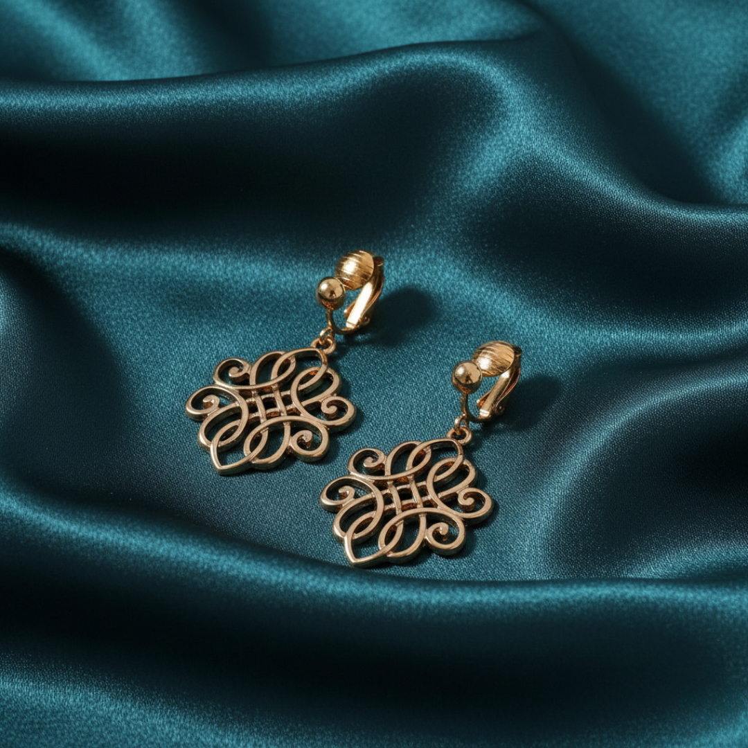 Gold earrings with intricate designs on a teal satin background