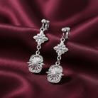 Silver floral earrings on a burgundy satin background