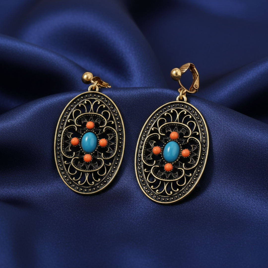 Ornate earrings with turquoise and orange stones on a blue satin background