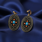 Ornate earrings with turquoise and orange stones on a blue satin background