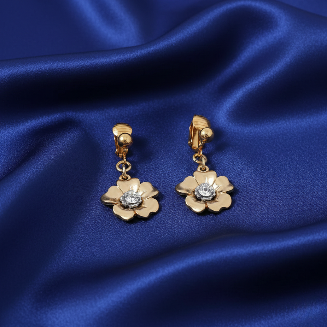 Gold flower-shaped earrings with a central crystal on a blue satin background