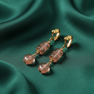 Gold earrings with pink crystals on a green fabric background