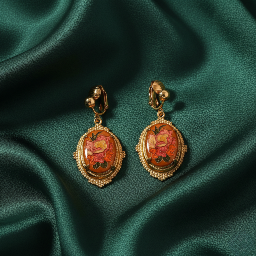Pair of gold earrings with floral design on a green satin background
