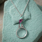 Neotropic Exotic Parrot  Amethyst & Blue Zircon Magnifying Glass Pendant Necklace on a teal stone surface