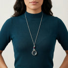 Woman in a dark blue sweater wearing a Neotropic Exotic Parrot  Amethyst & Blue Zircon Magnifying Glass Pendant Necklace 