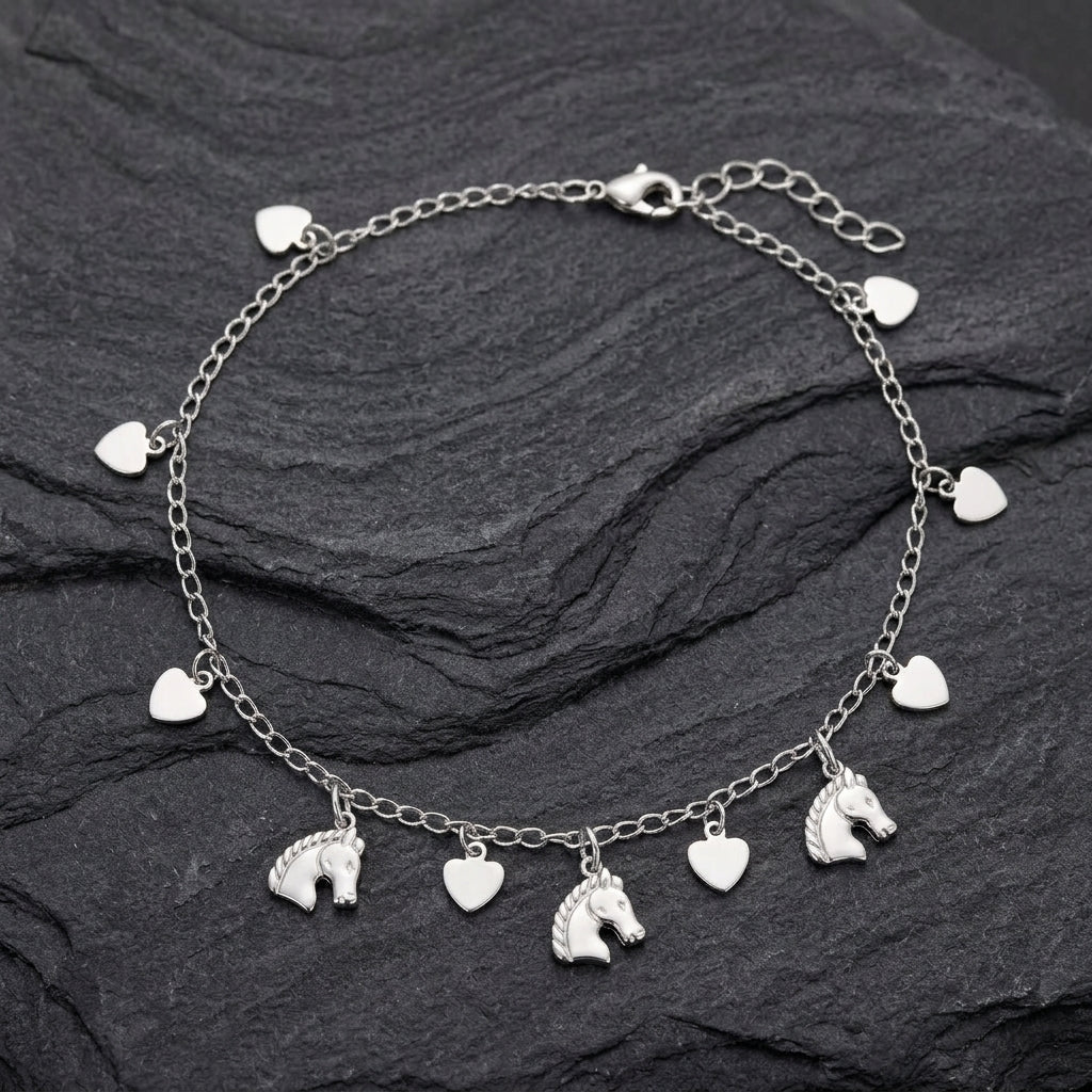 Silver anklet with horse and heart charms on a dark stone surface
