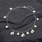 Silver anklet with horse and heart charms on a dark stone surface