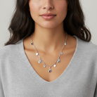Woman wearing a silver necklace with heart-shaped and horse-shaped pendants against a neutral background