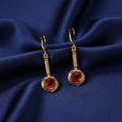 Gold earrings with red crystals on a blue satin background