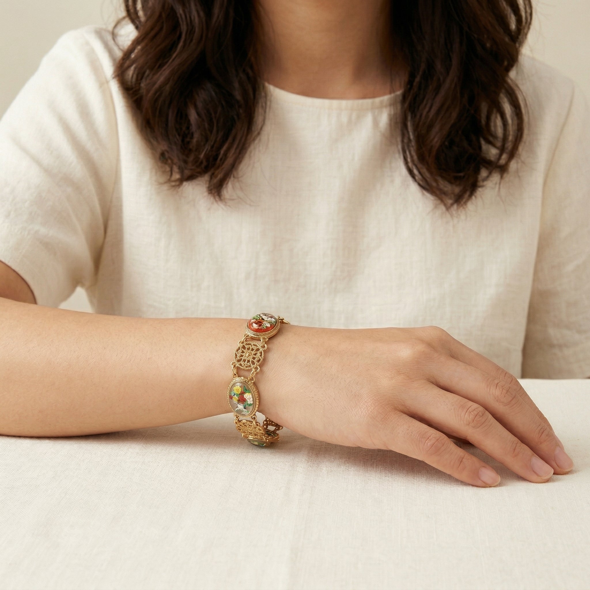 Close-up of a person wearing a gold tone Meso Round Intricate Filigree & Mixed Flower Bouquet German Glass Link Bracelet