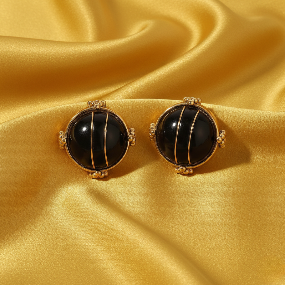 Pair of gold and black earrings on a yellow satin background
