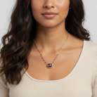 Woman wearing a gold necklace with a purple pendant against a neutral background