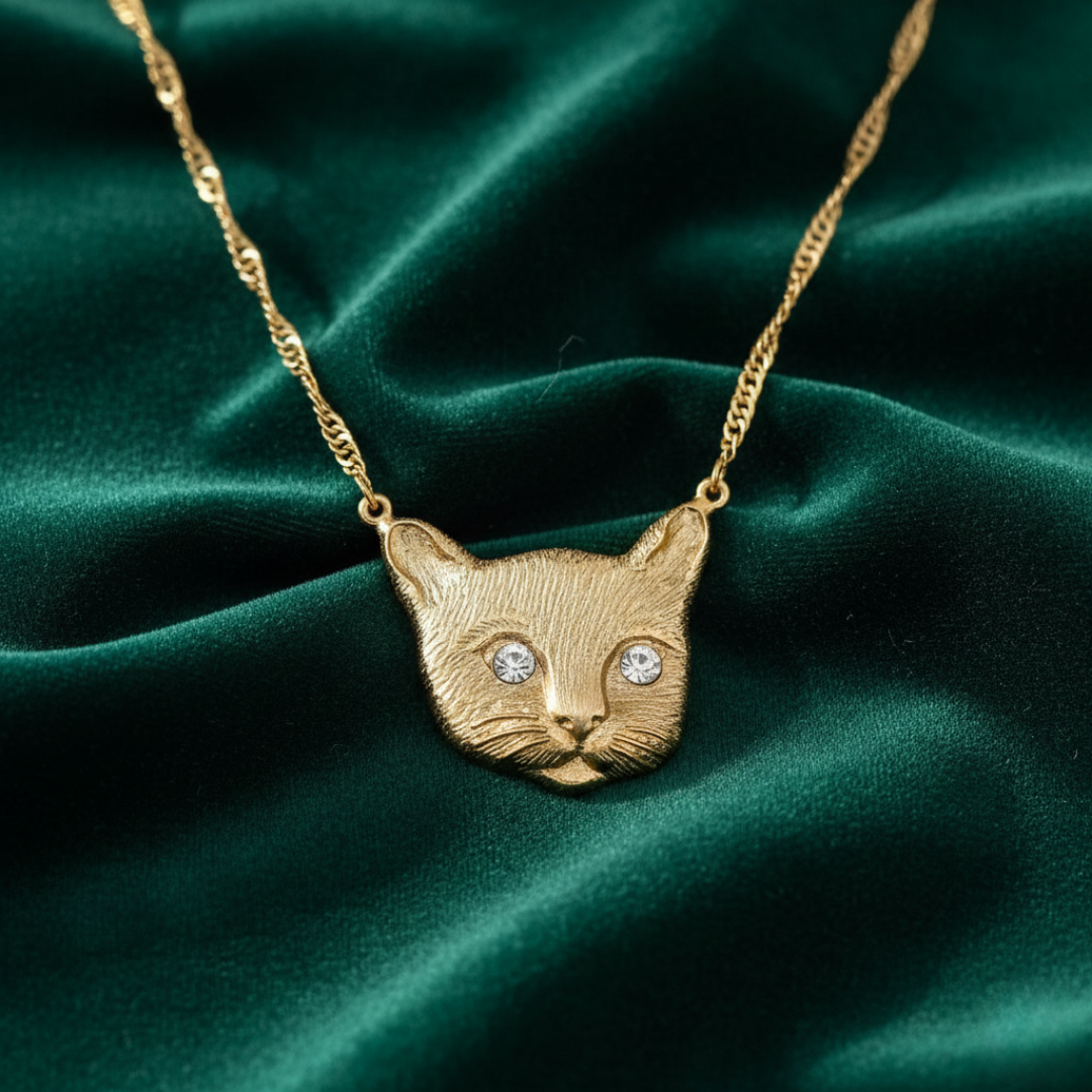 Gold cat-shaped pendant necklace on a green fabric background