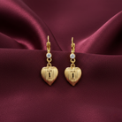 Gold heart-shaped earrings with crystals on a burgundy fabric background