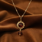 Gold necklace with a red gemstone pendant on a brown fabric background