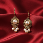 Pair of gold filigree earrings with faux pearls on a red fabric background