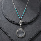 Turquoise Bead Equine Magnifying Glass Pendant Necklace resting on dark stone surface