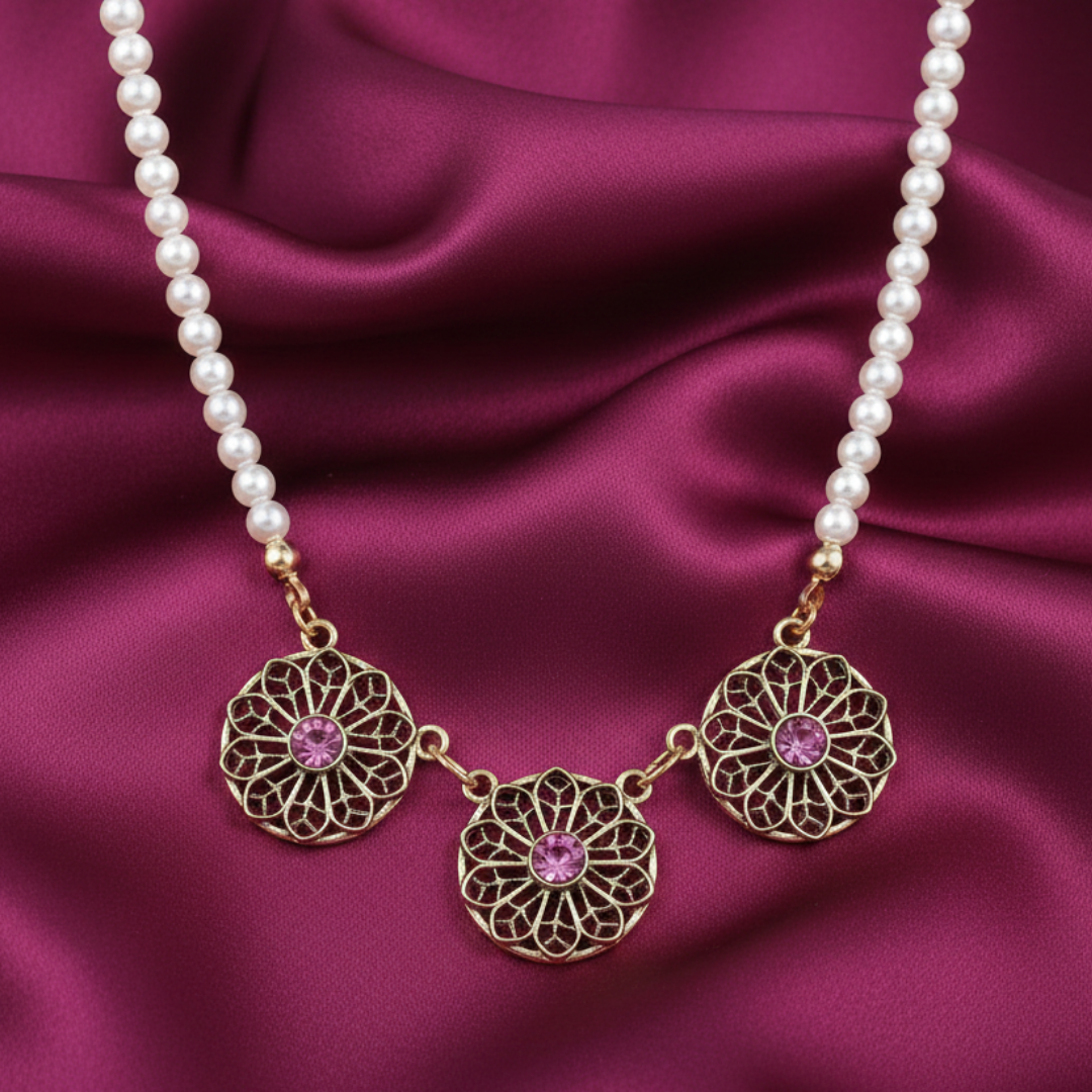 Faux pearl necklace with gold filigree pendants and pink gemstones on a purple satin background