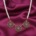 Faux pearl necklace with gold filigree pendants and pink gemstones on a purple satin background