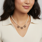 Woman wearing a faux pearl necklace with gold pendants on a neutral background