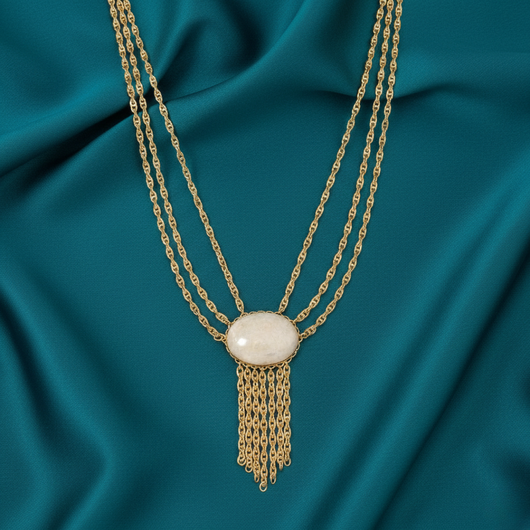 Gold necklace with a white pendant on a teal fabric background
