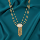 Gold necklace with a white pendant on a teal fabric background