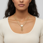 Woman wearing a gold necklace with a white pendant against a neutral background