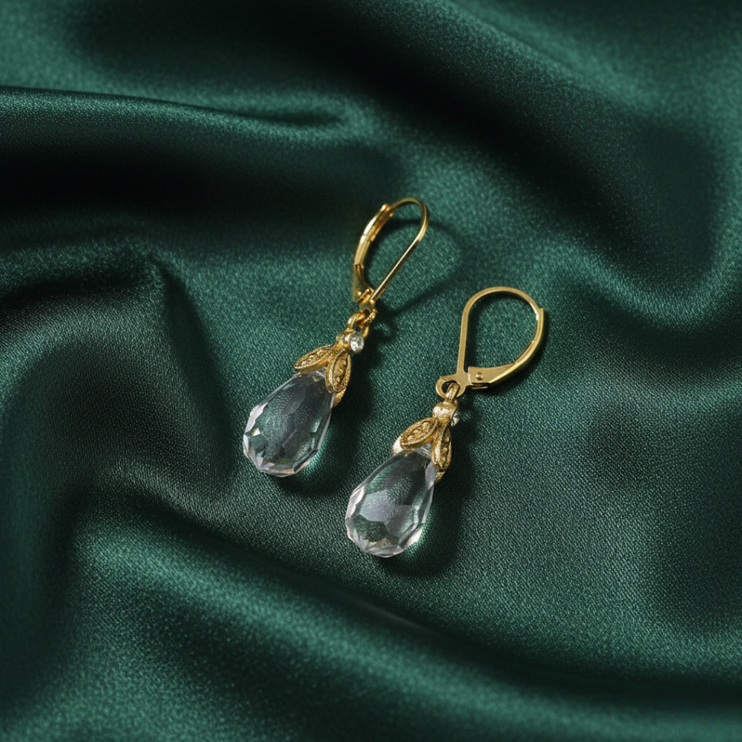 Gold earrings with clear teardrop-shaped crystals on a green satin background