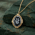 Gold necklace with a pendant featuring floral design outlined with four gold tone cats on a dark stone surface
