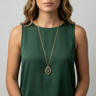 Woman wearing a green sleeveless top with a long oval pendant necklace against a neutral background