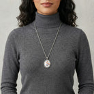 Person wearing a gray turtleneck sweater with a long necklace featuring a floral pendant.