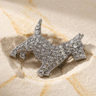 Silver dog-shaped brooch with crystals on a textured beige surface