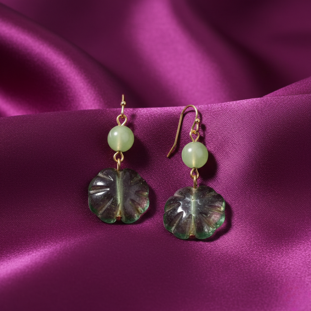 Pair of earrings with green beads and leaf-shaped glass drops on a purple fabric background