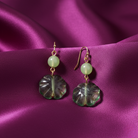 Pair of earrings with green beads and leaf-shaped glass drops on a purple fabric background