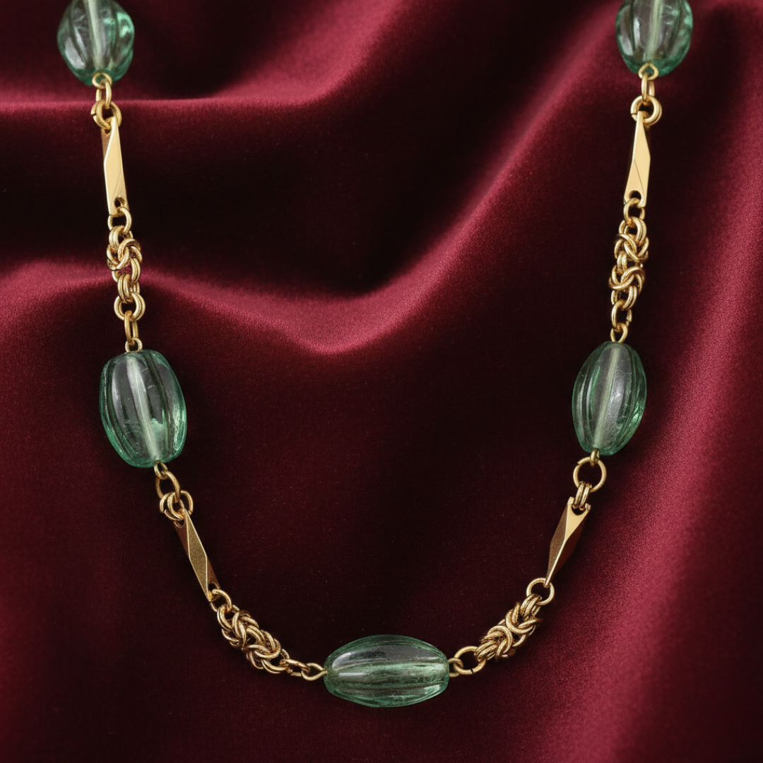 Gold necklace with green beads on a red fabric background
