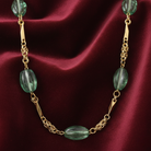 Gold necklace with green beads on a red fabric background