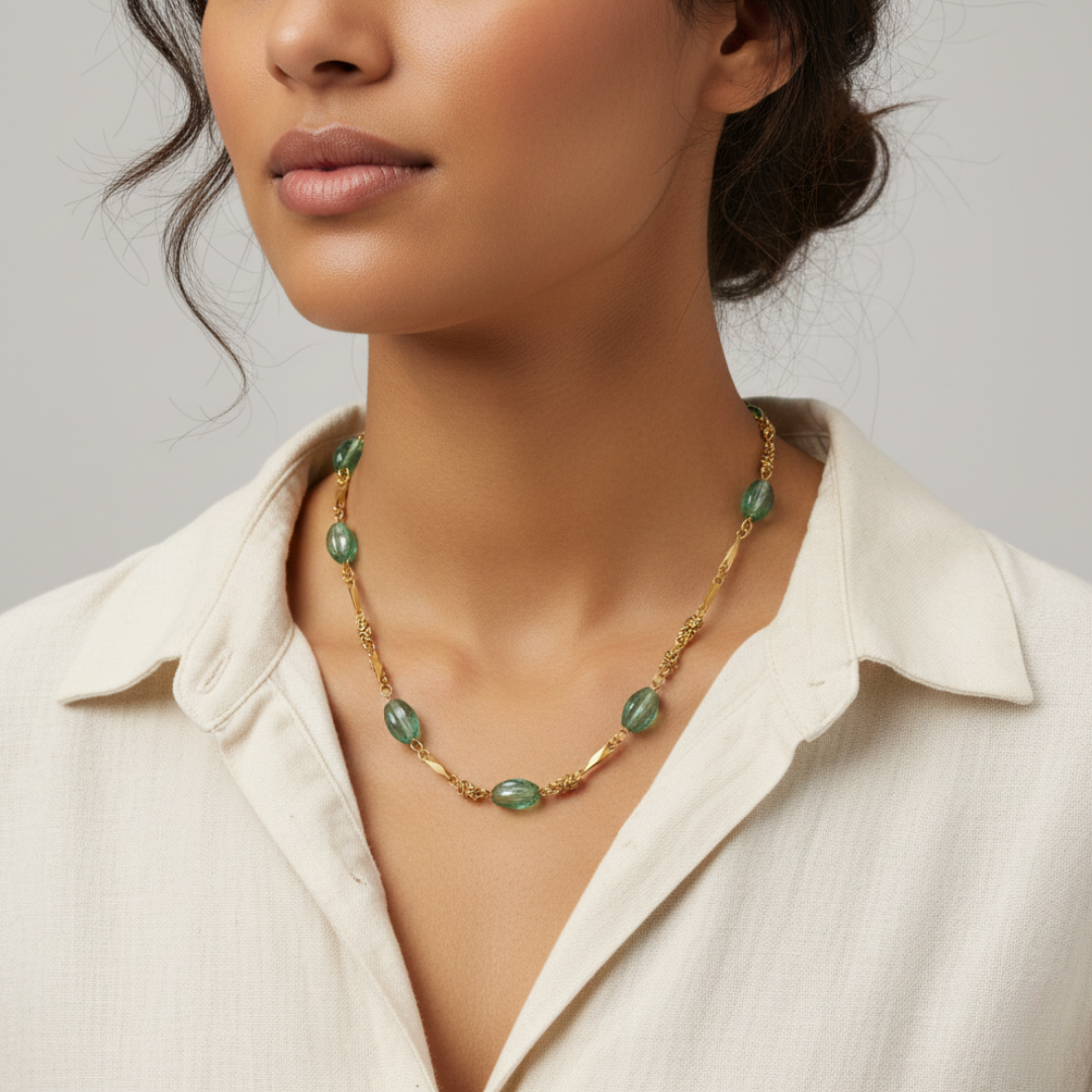 Woman wearing a gold necklace with green beads against a neutral background