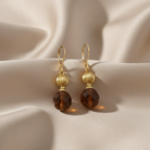 Gold earrings with brown crystals on a beige fabric background
