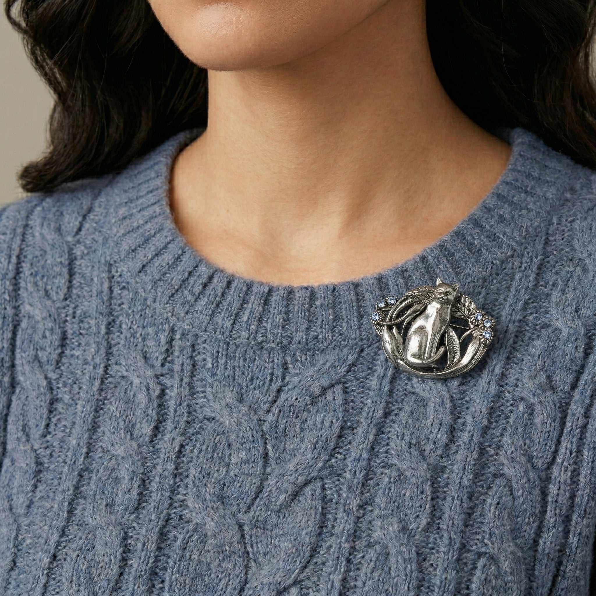 Silver cat brooch with blue crystal accents worn by a woman with a wool sweater