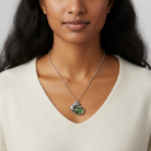 Woman wearing a necklace with a green pendant against a neutral background