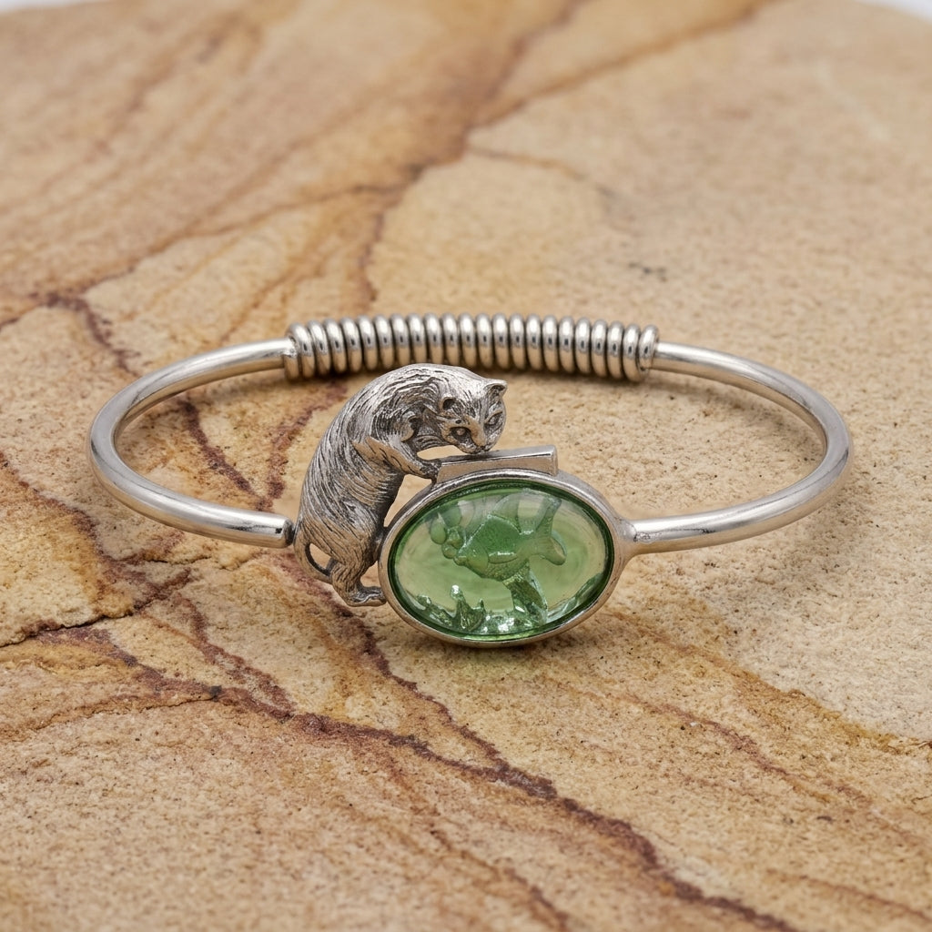 Silver bracelet with a green stone and cat and fish bowl design on a textured beige surface